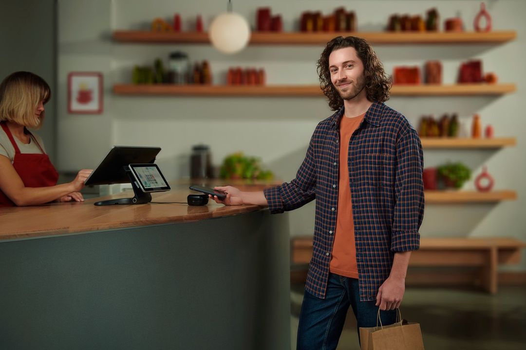 Man in flannel shirt paying with smartphone at the counter, cashier, digital POS, restaurant interior, contactless payment.